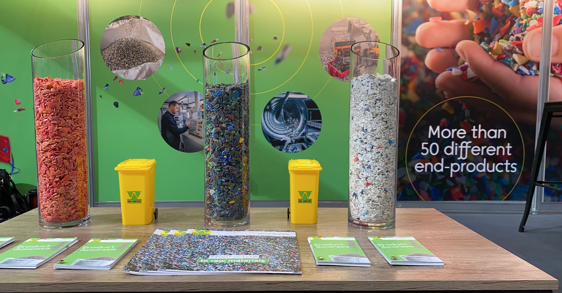 Beursstand van Van Werven met glazen cilinders vol gekleurde kunststofsnippers, miniatuurkliko's en productbladen