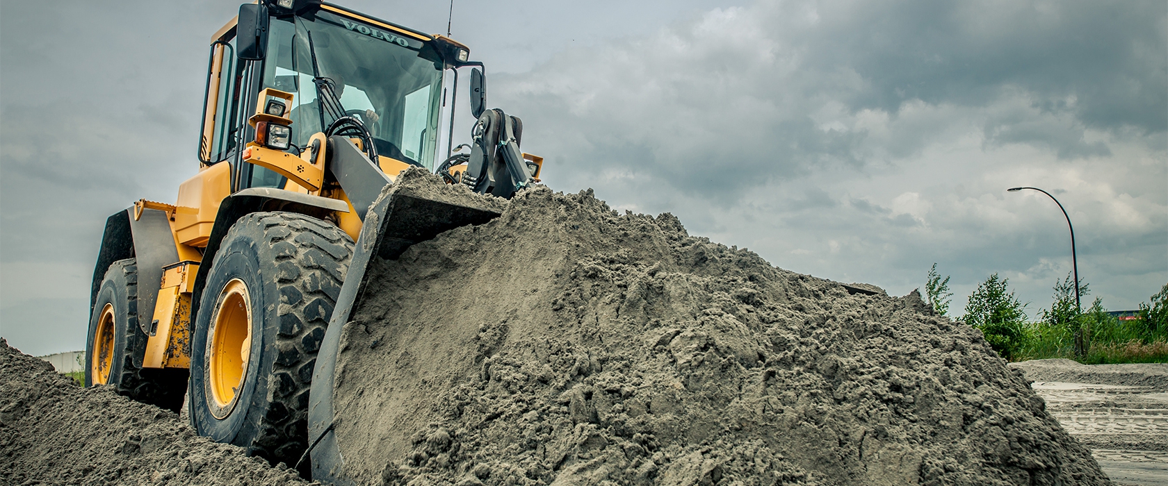 Wiellaadschop van Van Werven duwt een grote hoop zand op onder een donkere lucht