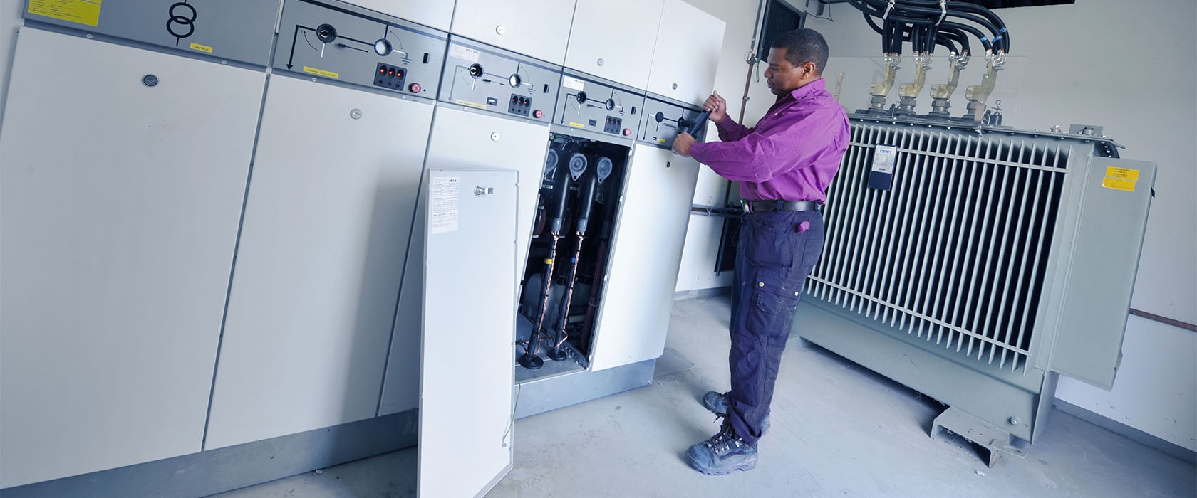 Een monteur bedient een schakelinstallatie naast een transformator in een Alfen-station