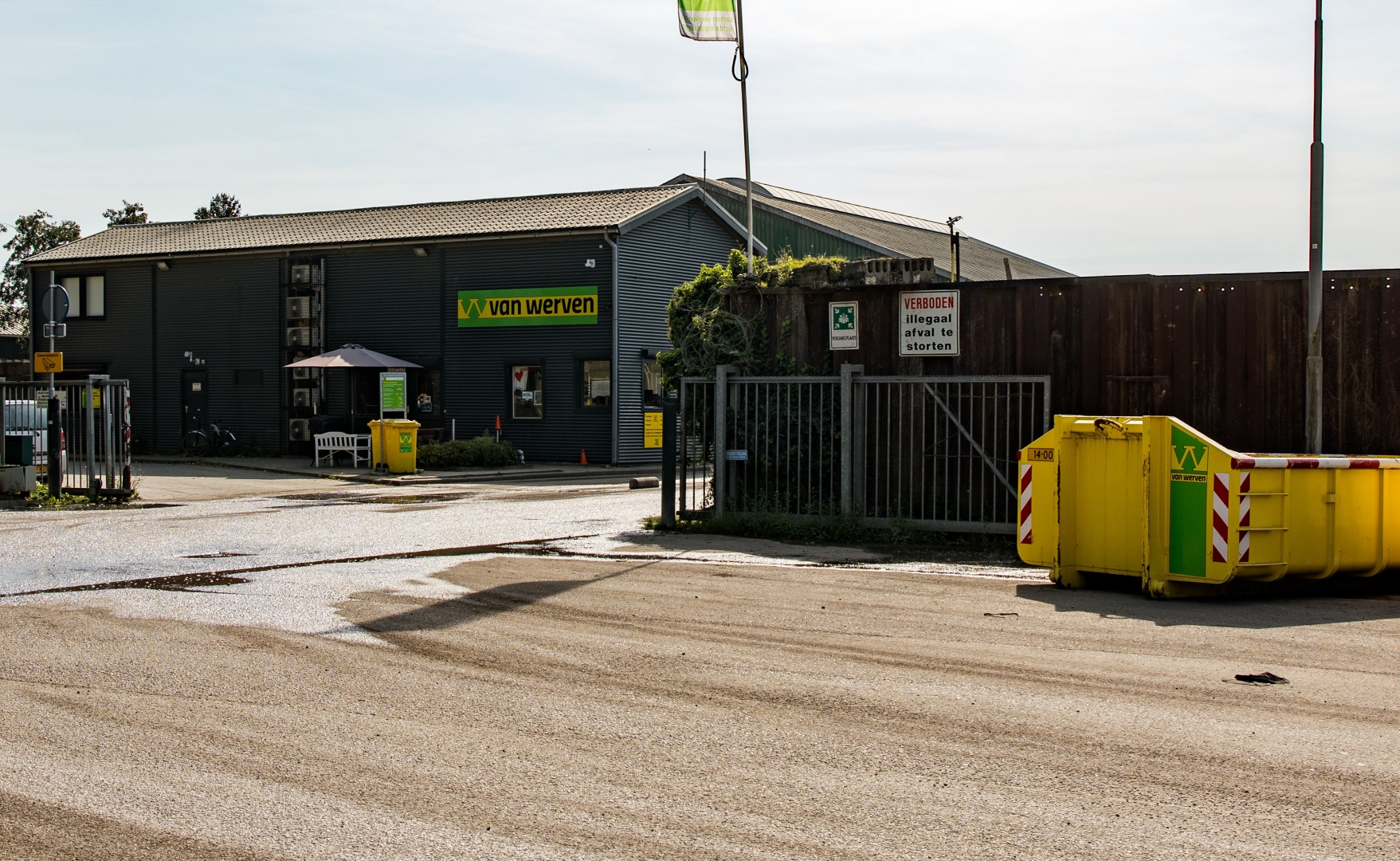 De ingang van de recyclingvestiging van Van Werven in Hattemerbroek, met het bedrijfspand, de gesloten toegangspoort en een gele afzetcontainer ernaast