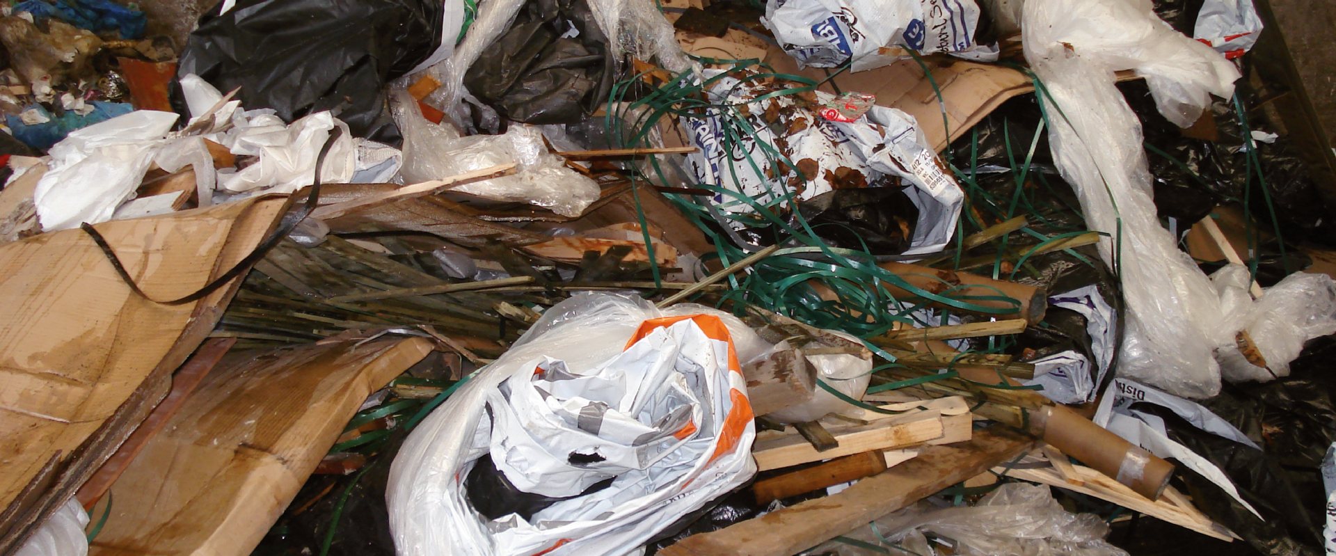 Gemengd bedrijfsafval van dichtbij: plastic folie, kartonnen dozen, houtresten, verpakkingen en groene bindbanden door elkaar in een container