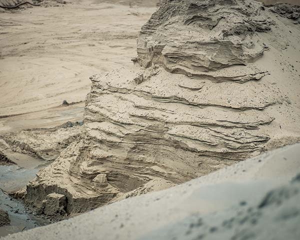 Afgegraven zandwand met horizontale lagen bij een zandwinlocatie, met water aan de voet