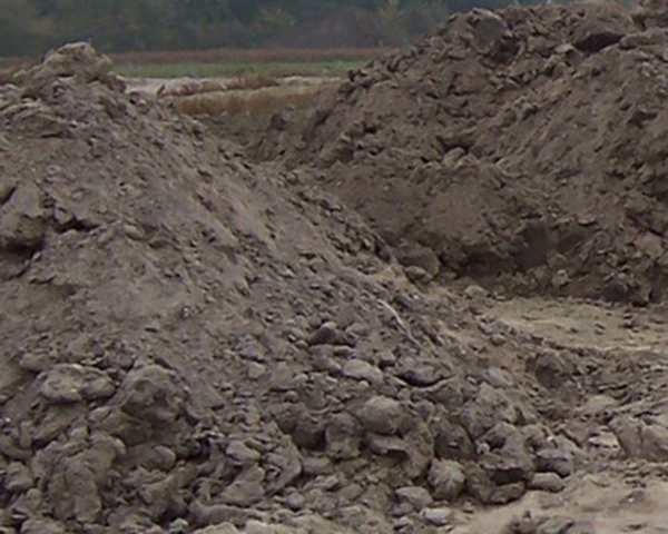 Hopen zware, kluiterige grond op een depot, met een akker en bomen aan de horizon
