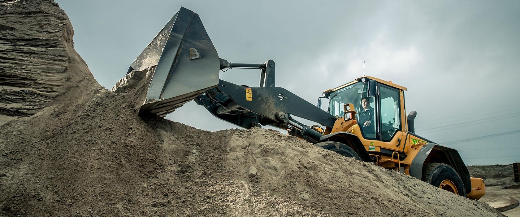Wiellader van Van Werven duwt zand omhoog op een zandberg bij een zandwinlocatie