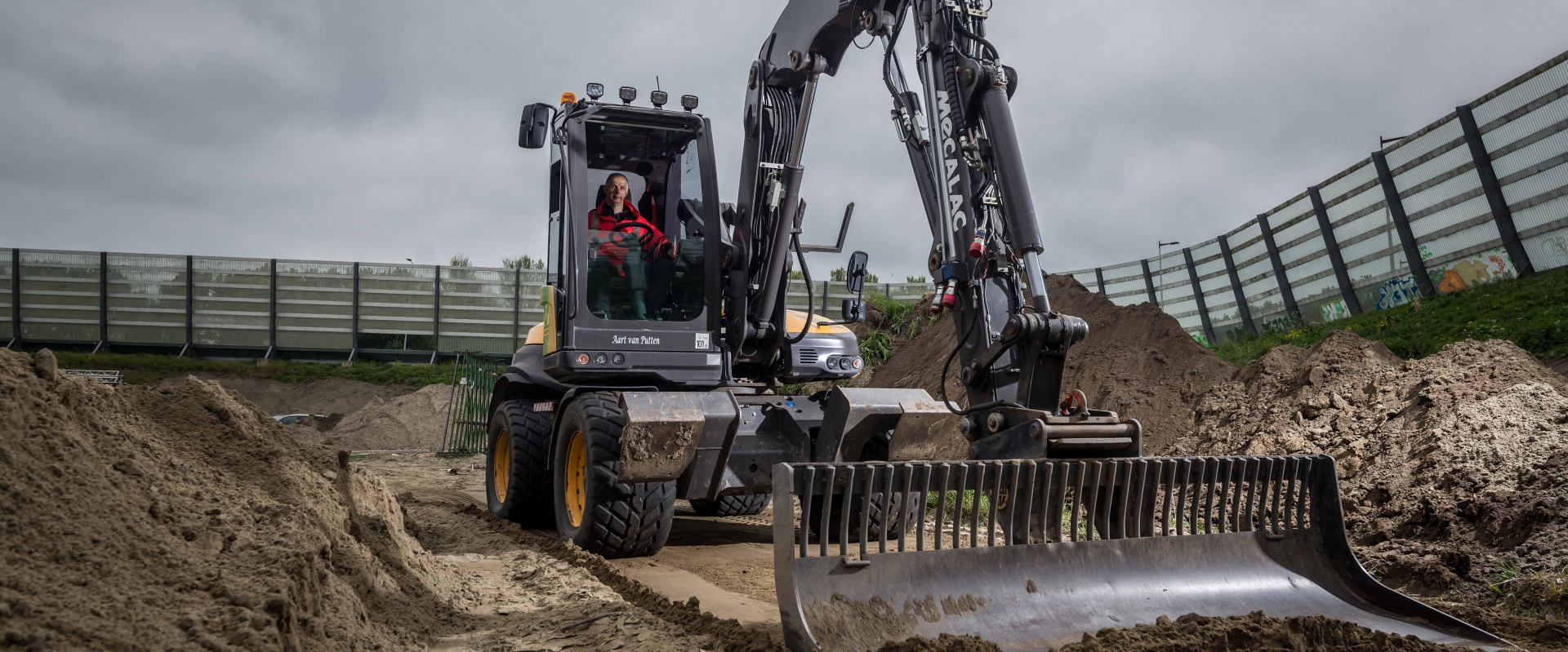 Mobiele graafmachine met kilverbak graaft een sleuf langs een geluidsscherm