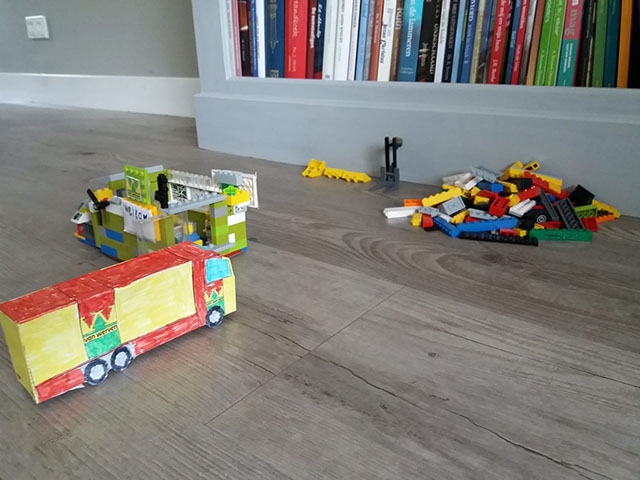 Zelfgemaakte vrachtwagen van karton in de kleuren van Van Werven, naast een truck van Lego en een hoop losse blokjes op de vloer